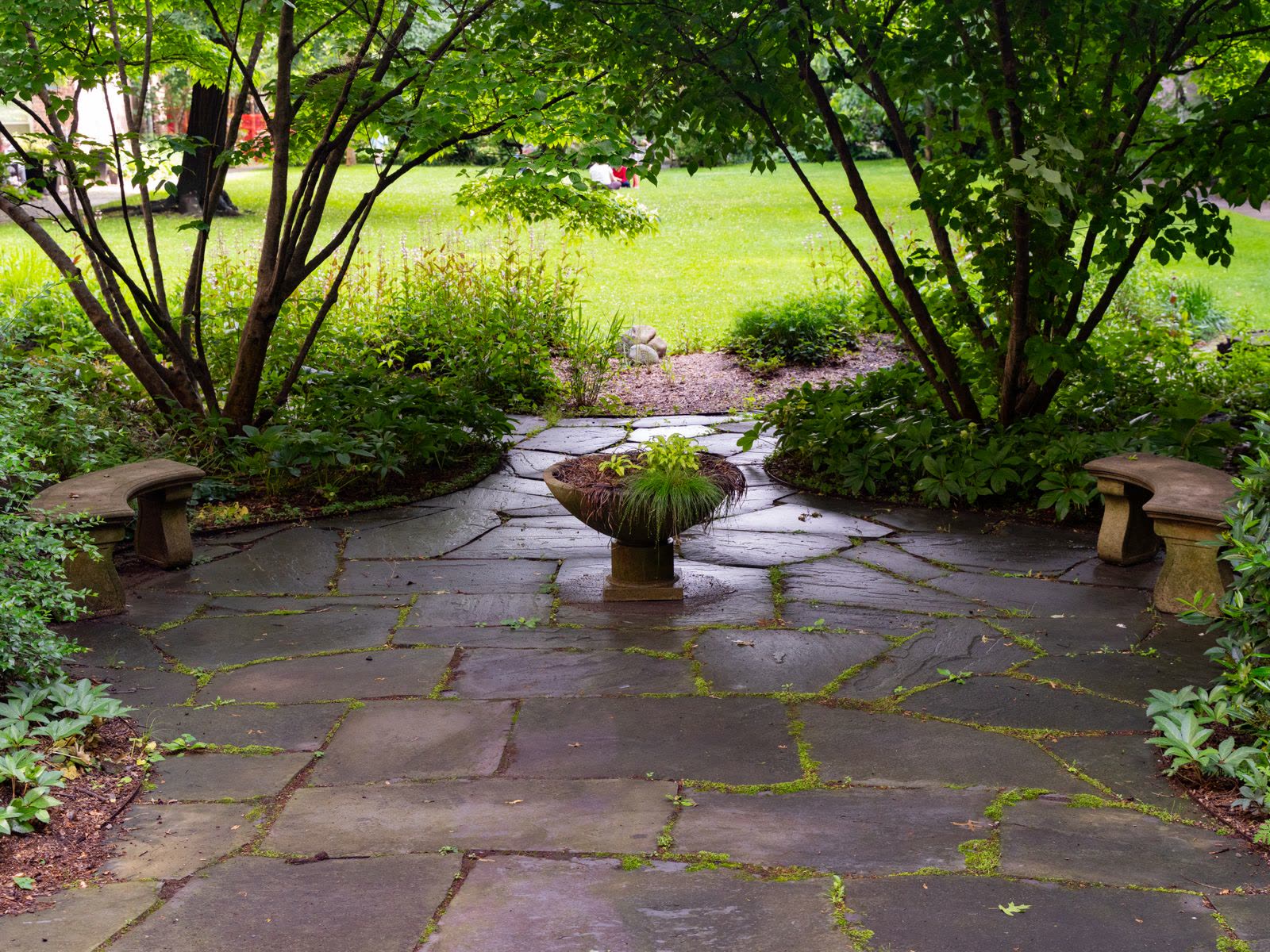 Natural flagstone patio with benches and a planter in a green garden