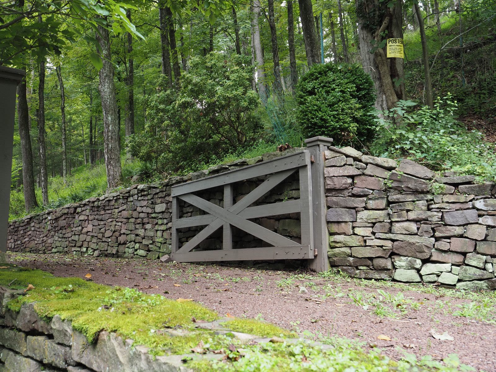 Dry-stacked stone retaining wall with a wooden gate in a forested setting